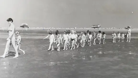 Kinder und Betreuerinnen beim Strandspaziergang. Historisches Foto.