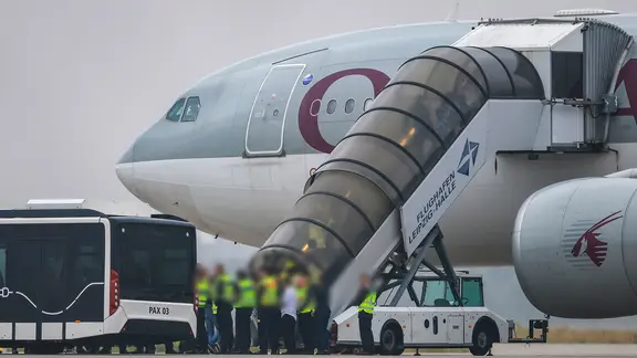 Menschen besteigen ein Flugzeug der Qatar Airways, vor dem Beamte der Bundespolizei stehen, auf dem Vorfeld am Flughafen Leipzig/Halle